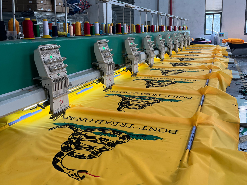 Multi-head embroidery machine stitching emblems onto yellow flag panels